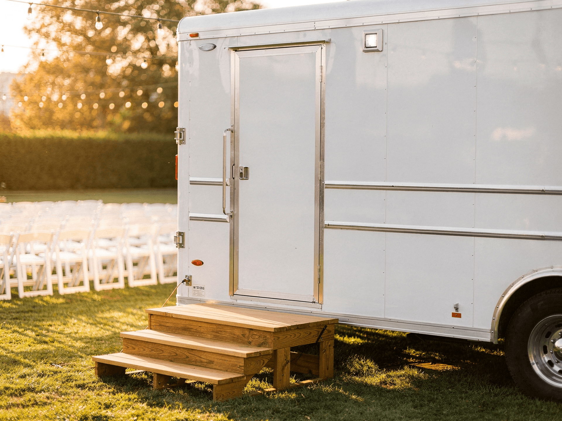 White luxury restroom trailer at an outdoor wedding venue with string lights